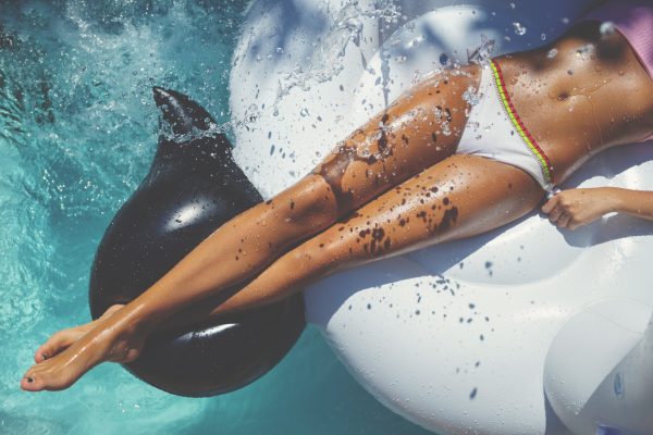 Woman Floating On A White Inflatable In Swimming Pool In A White Bikini.