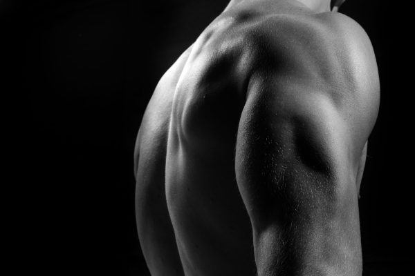 Male Fitness Model Showing Muscles In Studio With A Black Background